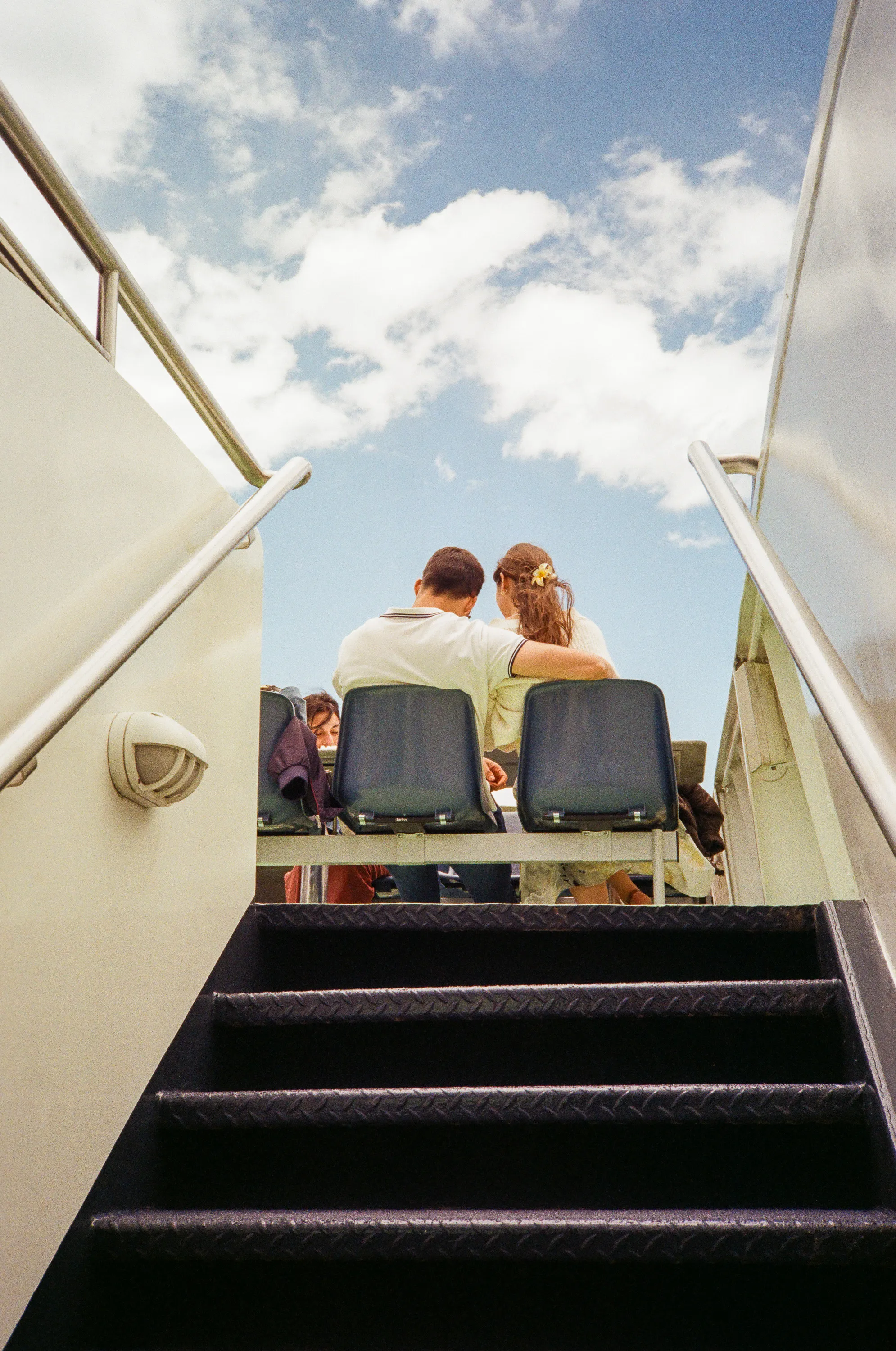 A couple seen from below up a boat stairway, his arm around her, a flower in her hair