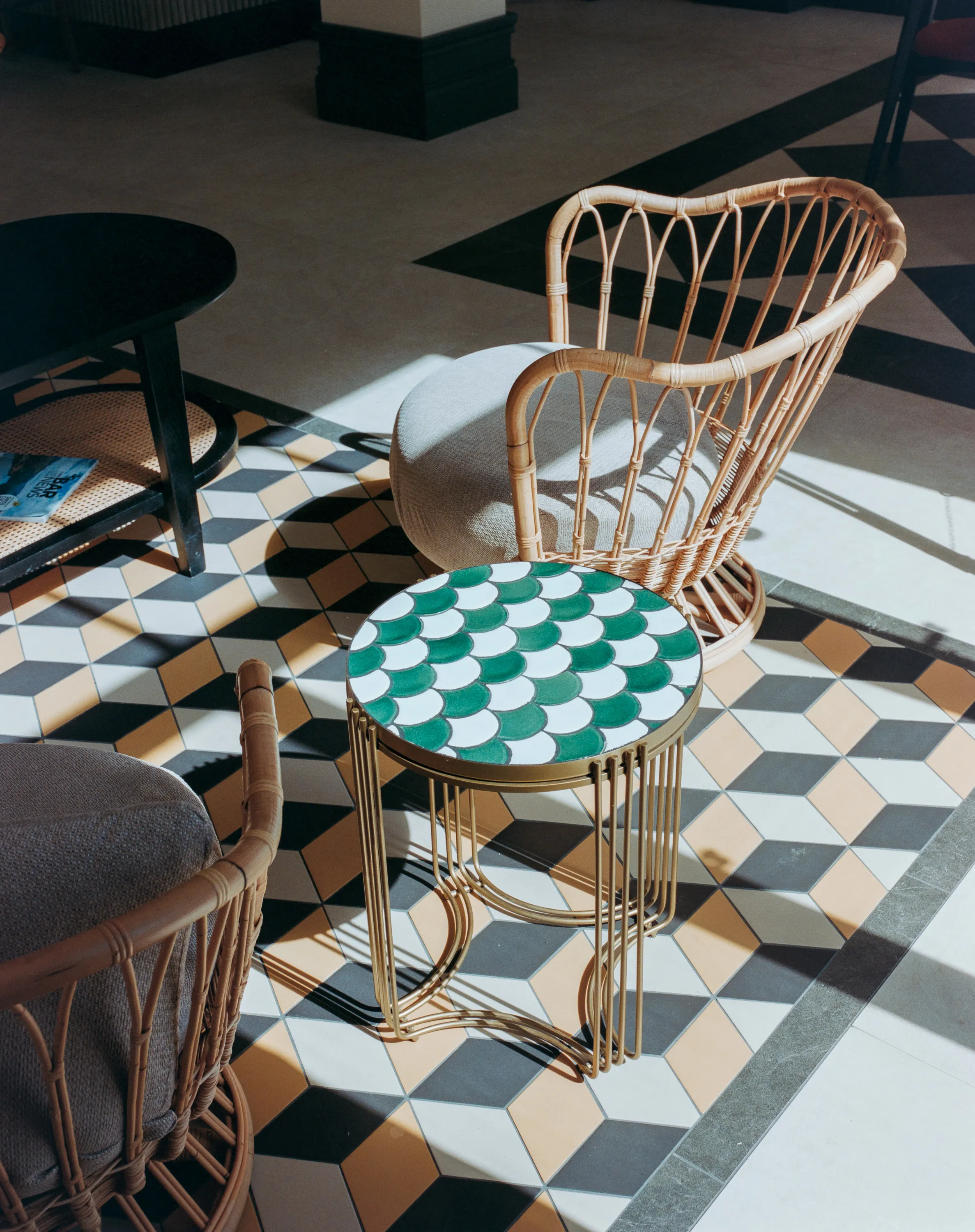 A rattan chair and a scale-tiled side table in hard sunlight on a geometric tiled floor
