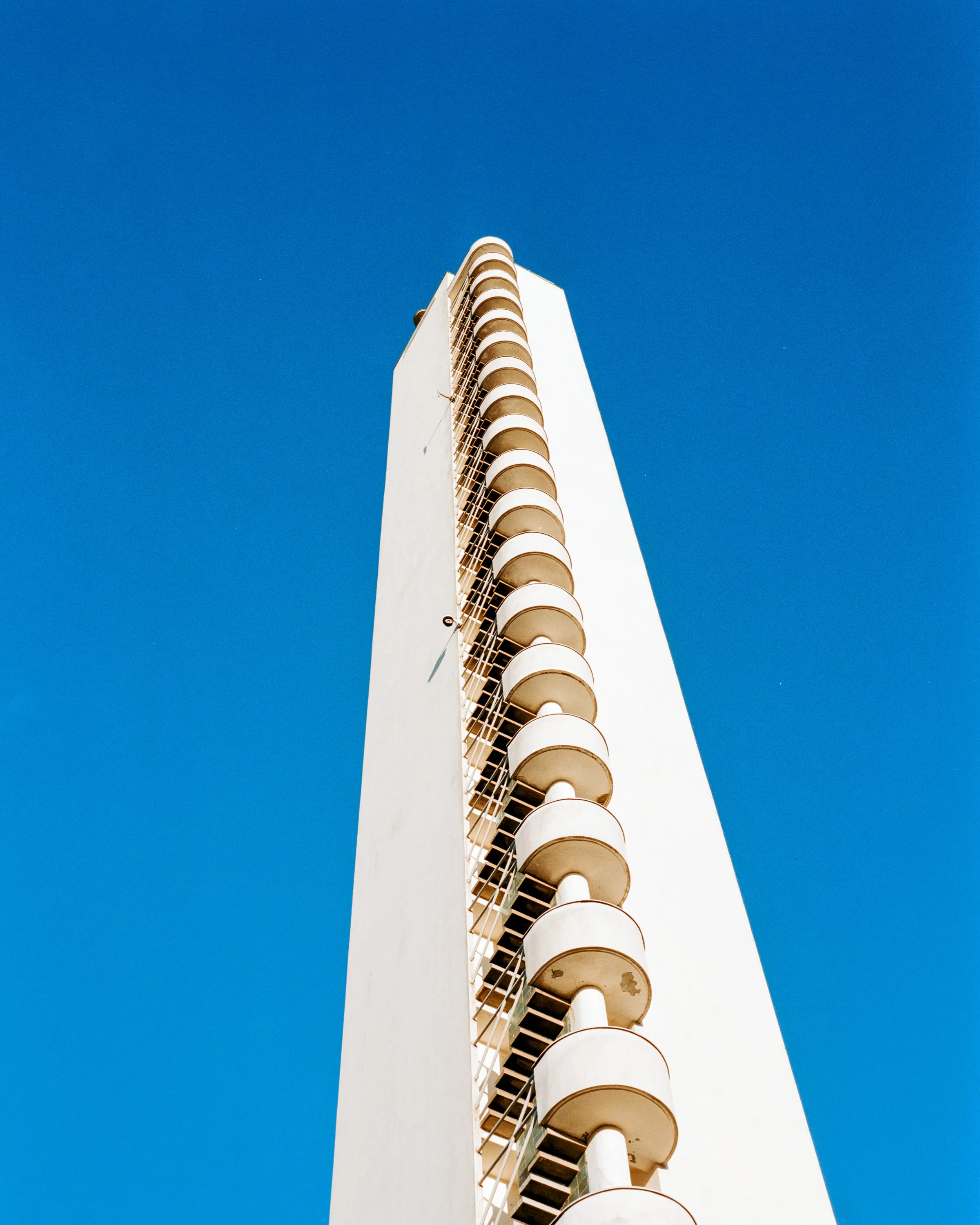 The Helsinki Olympic Stadium tower from below against a deep blue sky, stair landings stacked up its edge